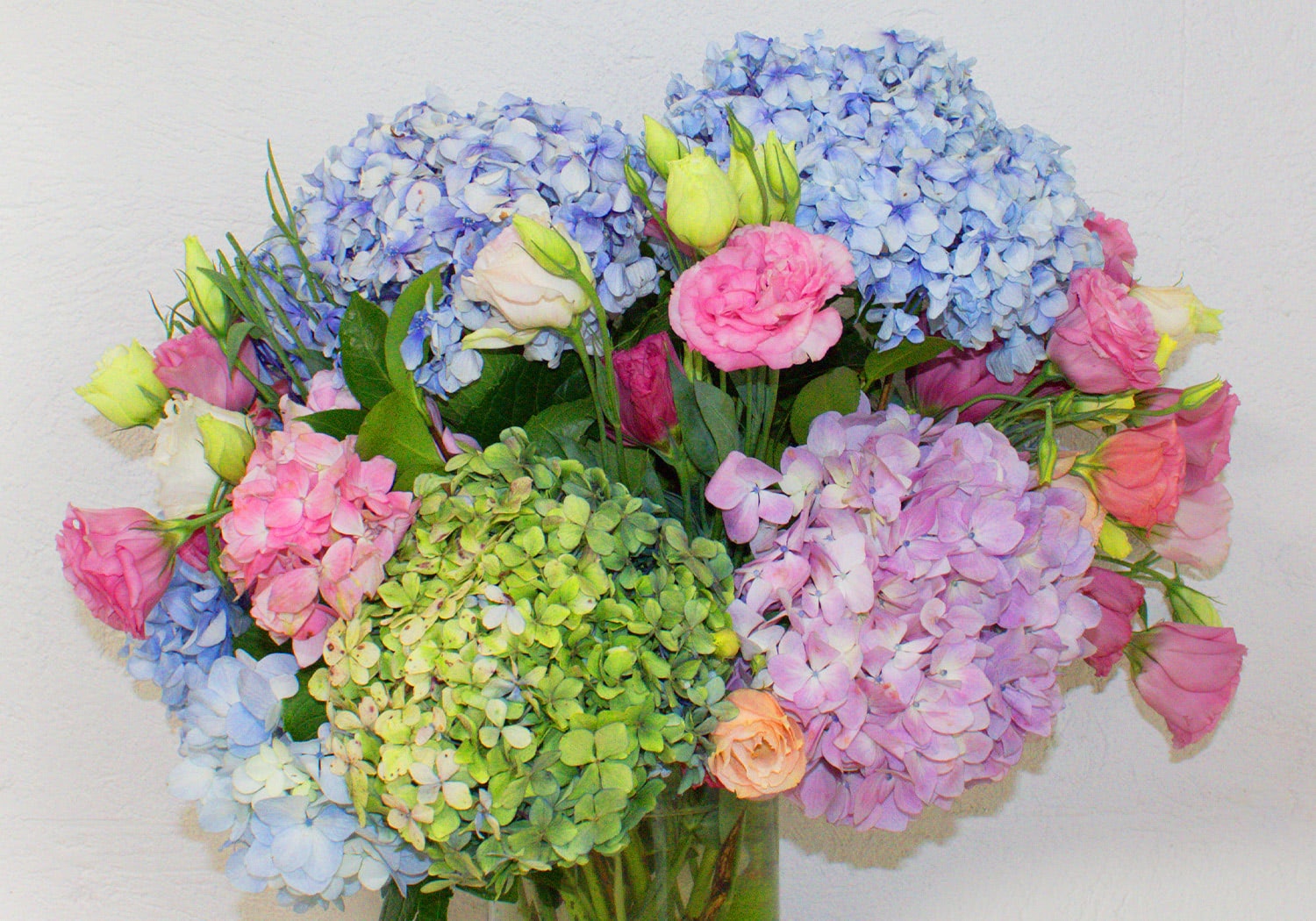 Blue, pink, and green spring bouquet with hydrangea, roses, and greenery in a clear glass vase.